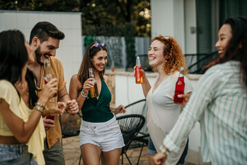 Group of diverse friends dancing and drinking during a pool party in a luxurious villa