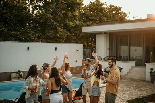 Group of diverse friends dancing and drinking during a pool party in a luxurious villa