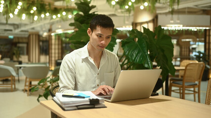 Concentrated businessman sitting at modern coworking space and working on laptop