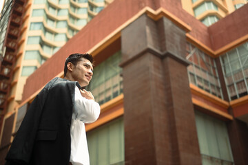 Attractive millennial businessman standing in an urban street with jacket on shoulder