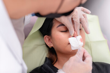 Plastic surgeon performing a nose thread lift on a young asian woman. The procedure aims to lift,...