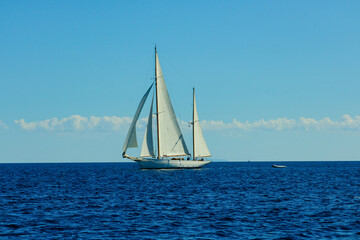 Fototapeta premium A sailboat is sailing in the ocean with a clear blue sky in the background