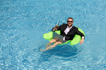 Crazy summer. Business drink summer cocktail and using laptop in suit in water pool. Fun business lifestyle. Funny middle aged business man dreams about summer. Summer travel. Business success.