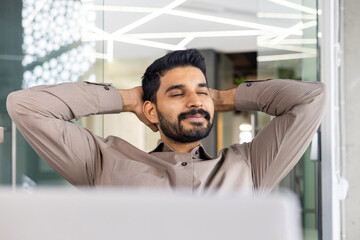 Smiling businessman relaxing with hands behind his head, enjoying a break in a modern office setting.