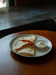 chicken quesadilla with simple minimalistic plating on round white plate, over wooden table background