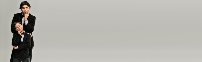 A father and son, both wearing tuxedos, stand side by side with thoughtful expressions.