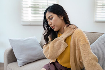 Woman Experiencing Shoulder Pain While Sitting on Sofa at Home, Holding Neck in Discomfort