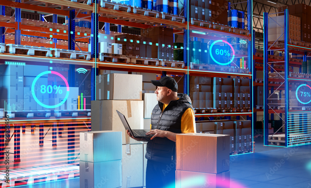 Poster man in innovation warehouse. monitor storage fullness via laptop. supervisor with computer stands in