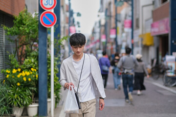 コンビニの袋を持って商店街を歩く男性