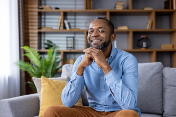 Smiling man relaxing at home on a couch. The comfortable and cozy living room interior provides a warm and welcoming atmosphere.