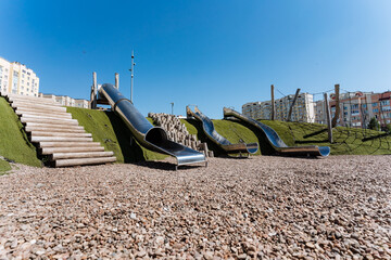 A playground in urban setting with slides and staircases amid cityscape on sloping asphalt ground, perfect for leisure activities. It blends into the landscape seamlessly