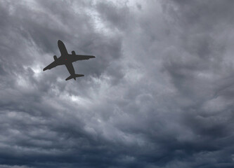 Silhouette of a holiday jet isolated flying against a dark stormy sky. No people. Copy space. Travel concept.