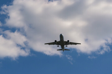 Unmarked passenger plane flying low with white clouds and a blue sky in the background