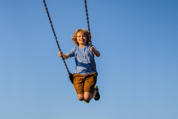 Child extreme swinging. Danger high Swing in sky. Cute child having fun on a swing on summer sky background. Blonde little boy swings at kid playground. Child swinging high.