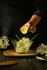A chef hand squeeze sliced lemon into a bowl of elderflowers before preparing a healthy and tasty...