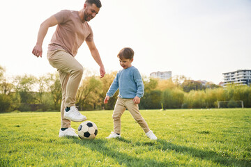 Playing soccer. Happy father with son are having fun on the field at summertime