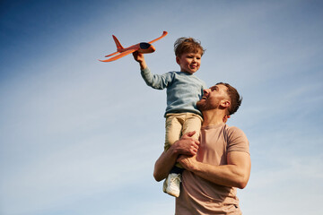 Blue sky with white cloud. Father is holding son that playing with toy plane