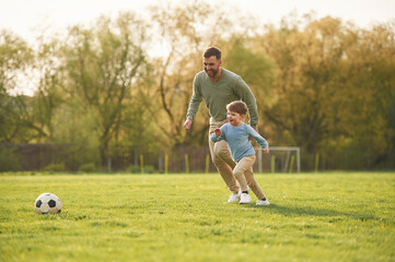 With soccer ball. Happy father with son are having fun on the field at summertime