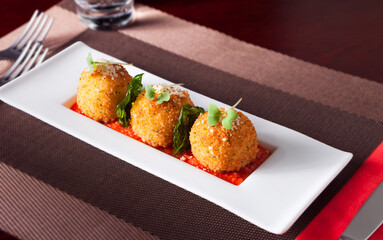 Appetizer of cheese balls in a tomato sauce in a white plate garnished with micro greens