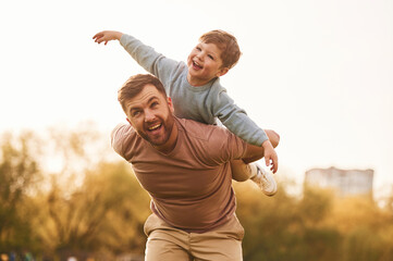 Conception of imagination, sitting on shoulders and flying. Happy father with son are having fun on...