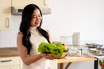 woman enjoying cooking in the kitchen, preparing her healthy salad, posing with a tomato. home cooking, healthy lifestyle, wellness eating, weight loss recipes