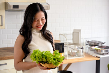 woman enjoying cooking in the kitchen, preparing her healthy salad, posing with a tomato. home cooking, healthy lifestyle, wellness eating, weight loss recipes