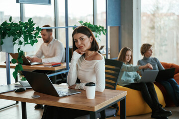 Obraz premium Young woman is sitting and posing. People are working in the office with bean bags chairs in it