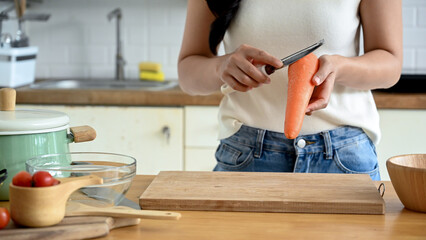 A cropped image with a copy space, A woman peeling a carrot with a knife, cooking at the kitchen table in the kitchen. home cooking, healthy lifestyle, wellness eating