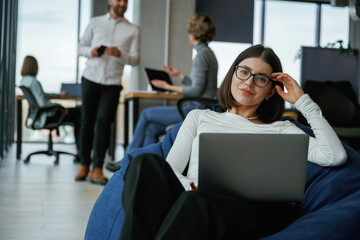 Naklejka premium Smart woman is sitting and uses laptop. People are working in the office with bean bags chairs in it
