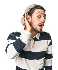 Young Caucasian man in studio setting trying to listening a gossip.