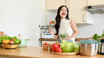 Portrait of pretty young woman eating fresh salad from in modern kitchen. Wellbeing and healthy lifestyle concept