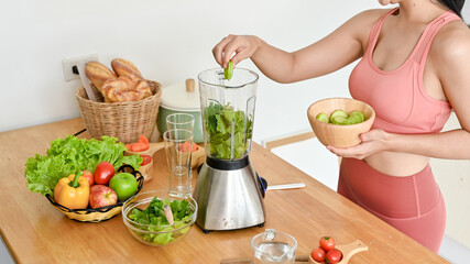 Smiling young woman making smoothie with fresh vegetables in kitchen. Healthy lifestyle concept.