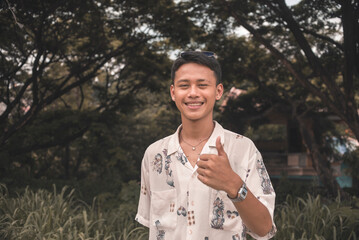 Young asian man in boho fashion outdoors smiling and giving thumbs up