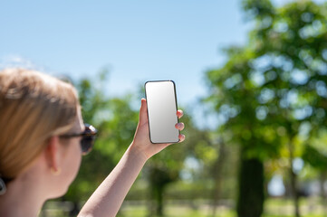 Teen girl takes a photo of a beautiful landscape or a selfie on her smartphone in a city park on a sunny summer day.