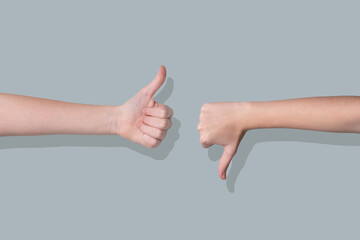 Two hands showing thumbs up and thumbs down gestures on a gray background.