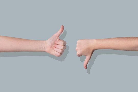 Two hands showing thumbs up and thumbs down gestures on a gray background.