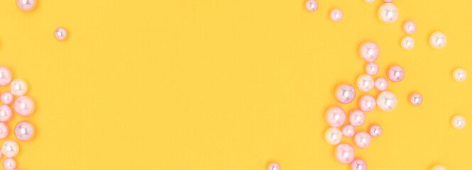 Imitation pearl beads scattered on a yellow background. Banner with copy space.