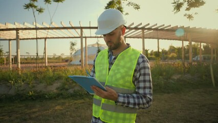 Focused Caucasian man businessman architect male guy engineer hardhat uniform pointing finger showing gesture park checking inspect project writing clipboard looking around construction village meadow