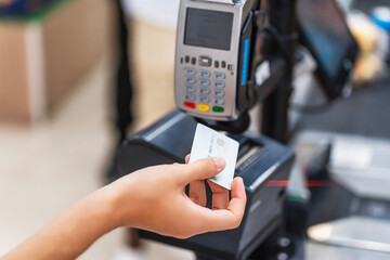 Close-up of a customer's hand using a credit card to pay a cashier at the checkout counter in a supermarket, cashless money and credit card payment technology concept.
