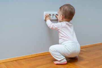 Baby hand reaching for an electrical outlet covered with safety plugs