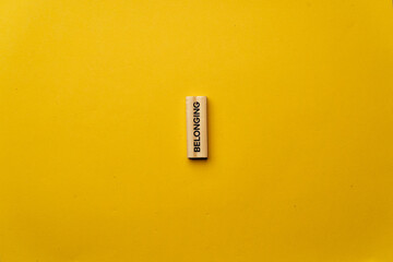 a yellow warm background without shadows wooden cubes with black letters laid out word belonging
