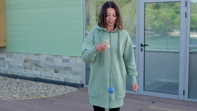 A young woman is joyfully playing with a kendama outside. A kendama is a traditional Japanese toy consisting of a ball connected by a string to a handle with three cups and a spike