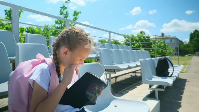 Back to school. Elementary school student. First grader. The beginning of classes. A little girl with a backpack is sitting on a bench, holding textbooks in his hands.