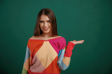Showing by hand to the side, place for text. Young woman is standing against green background in the studio
