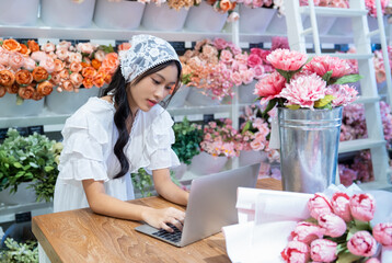 Small flower shop owner florist. Female Florist gardener working on laptop and taking online orders in store