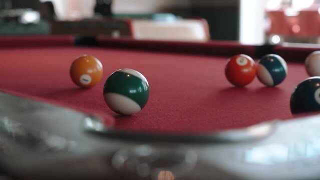 A billiard player hits a ball with a cue stick on an orange table in a sports pub and hits the pocket close-up