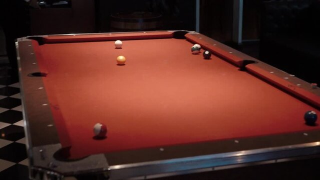 A billiard player hits a ball with a cue stick on an orange table in a sports pub and hits the pocket close-up