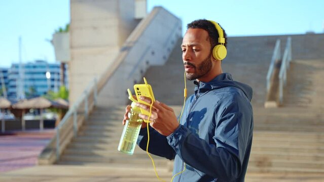 A male runner takes a break to drink water while using an app on the smartphone.