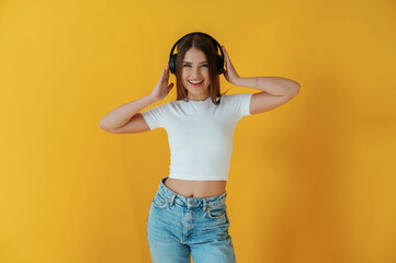 In headphones, enjoying music. Young woman is against yellow background