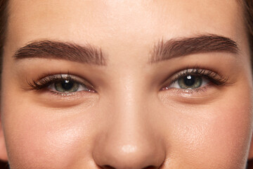 Obraz premium Cropped close-up image of female face, eyes, brows, nose. Well-kept smooth skin, perfect brows. Lash lamination. Smiling face. Natural beauty, skincare, cosmetology and cosmetic products ads concept